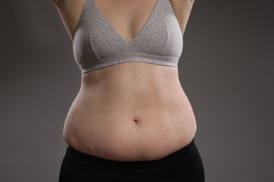 Woman with excessive belly fat on grey background, closeup. Overweight problem