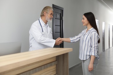 Photo of Senior doctor shaking hands with patient in hospital hall