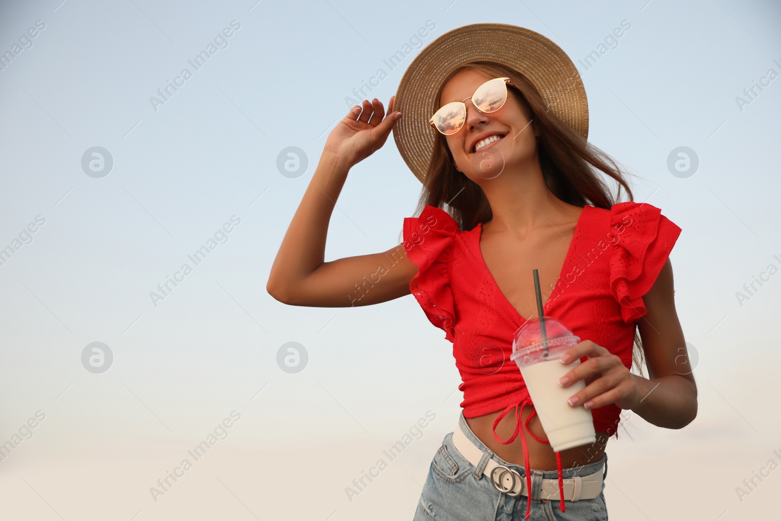 Photo of Beautiful young woman with tasty milk shake outdoors, space for text