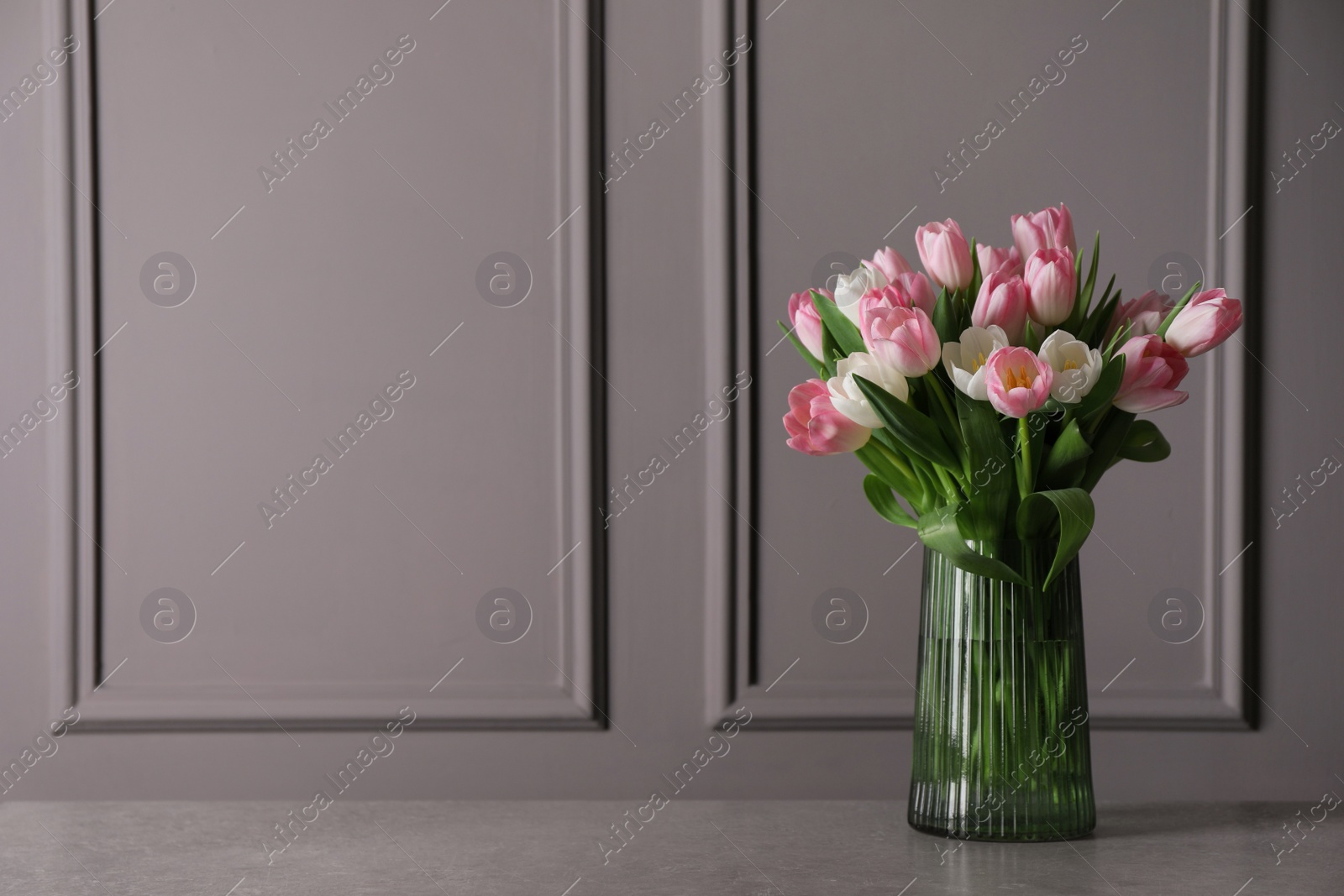 Photo of Beautiful bouquet of tulips in glass vase on grey table. Space for text