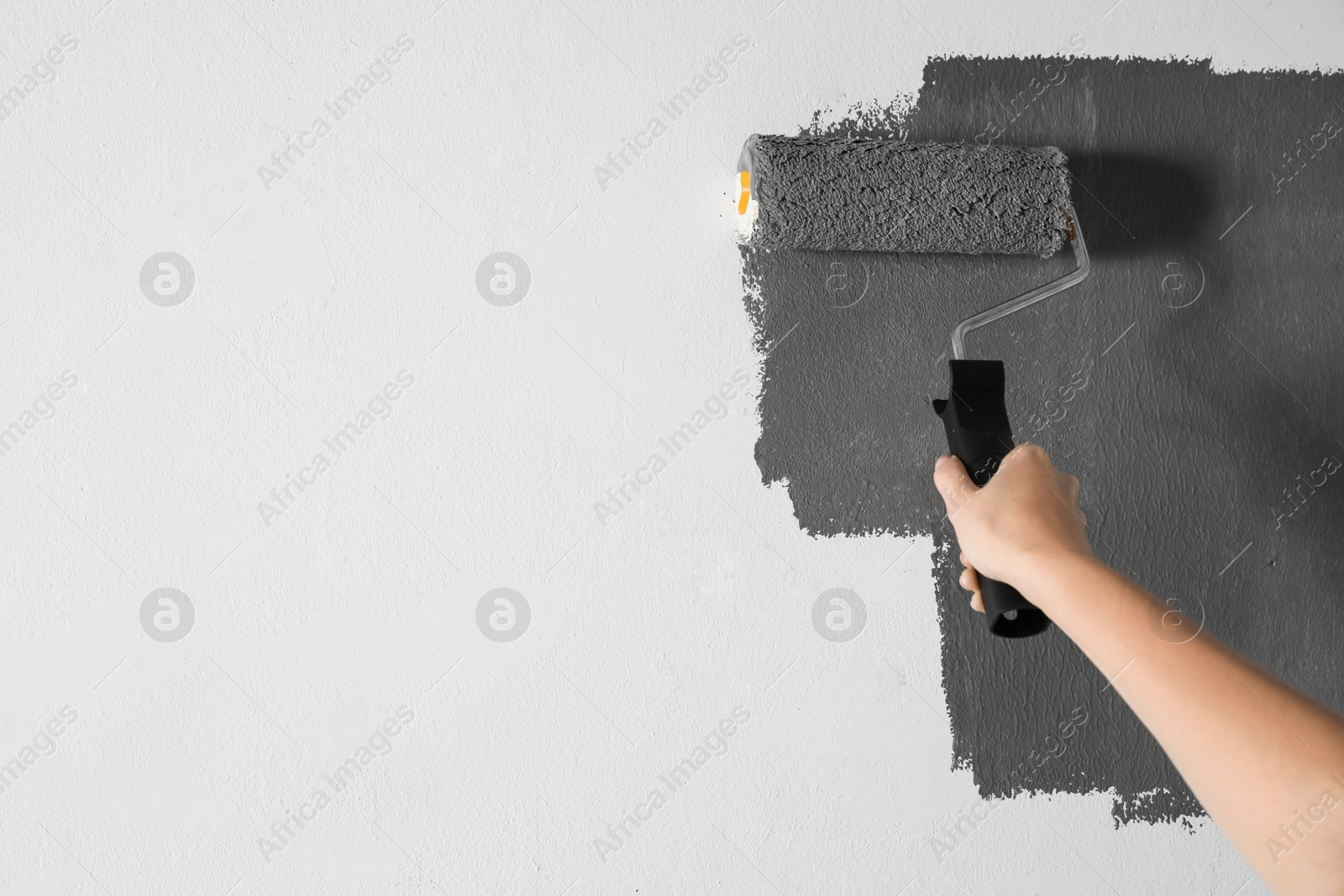 Photo of Woman painting white wall with grey dye, closeup. Space for text