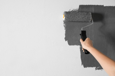 Photo of Woman painting white wall with grey dye, closeup. Space for text