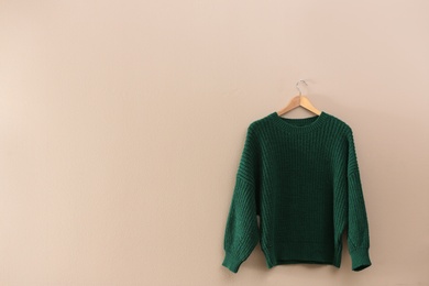 Photo of Hanger with stylish sweater on beige wall. Space for text