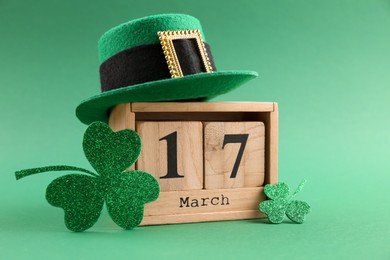 St. Patrick's day - 17th of March. Wooden block calendar, leprechaun hat and decorative clover leaves on green background