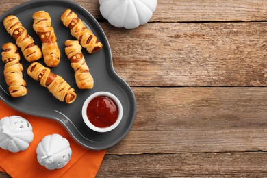 Photo of Cute sausage mummies served with ketchup on wooden table, flat lay with space for text. Halloween party food