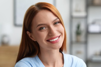 Portrait of beautiful young woman with red hair at home. Attractive lady smiling and looking into camera