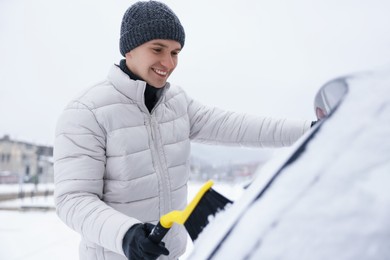 Photo of Man cleaning snow from car with brush outdoors