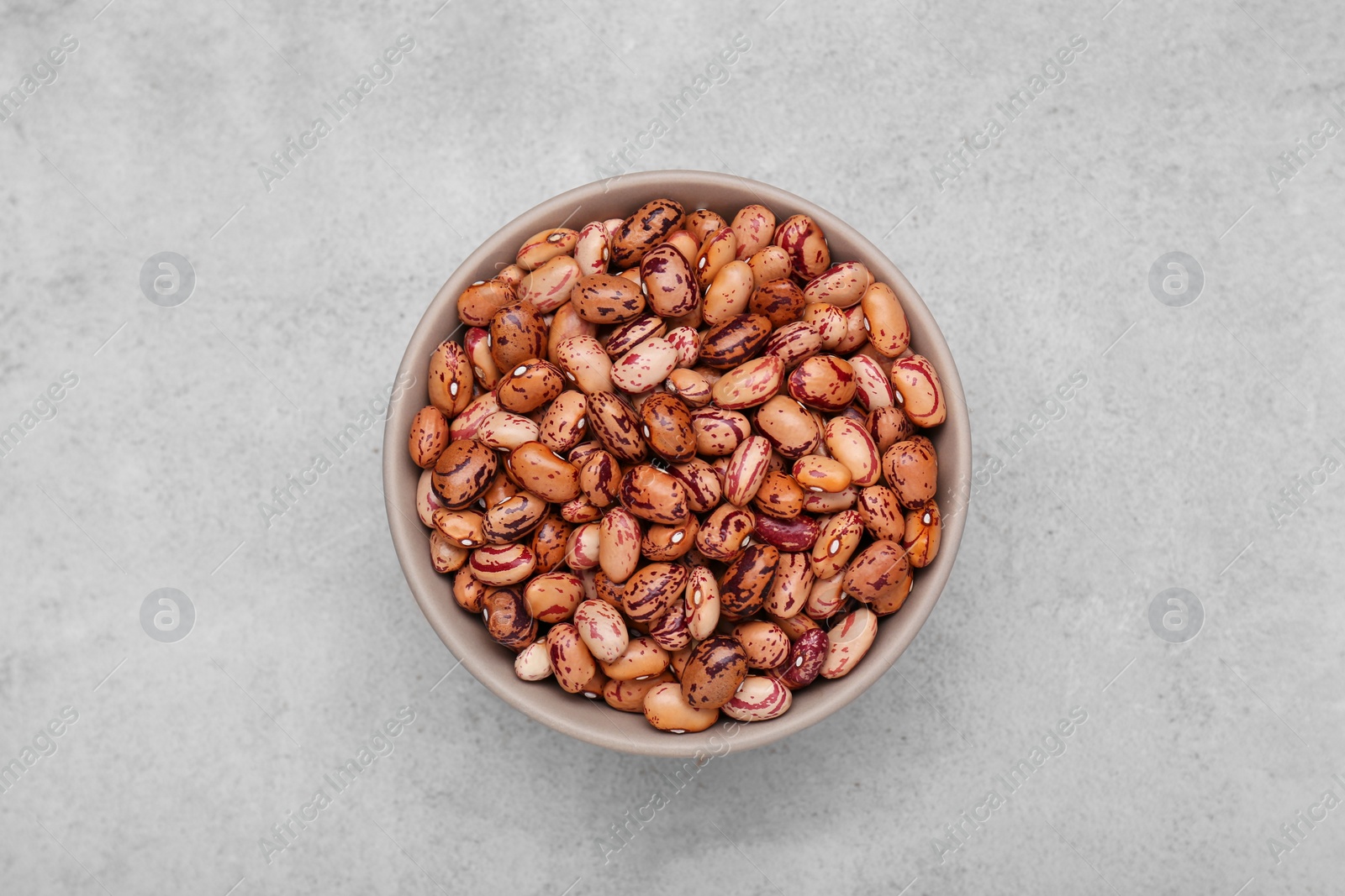 Photo of Bowl with dry kidney beans on light grey table, top view