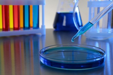 Photo of Dripping blue liquid into Petri dish on grey table in laboratory, closeup. Space for text