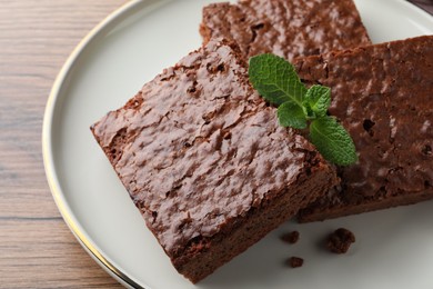 Photo of Delicious chocolate brownies with fresh mint on wooden table, closeup