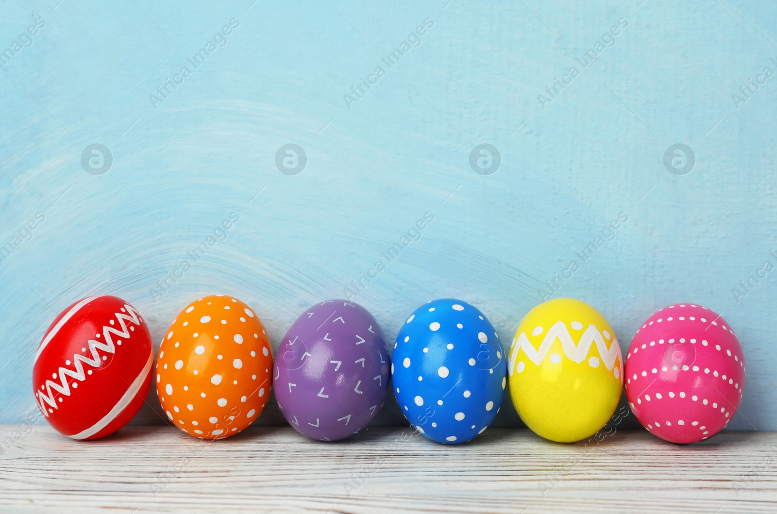 Photo of Decorated Easter eggs on table near color wall. Space for text