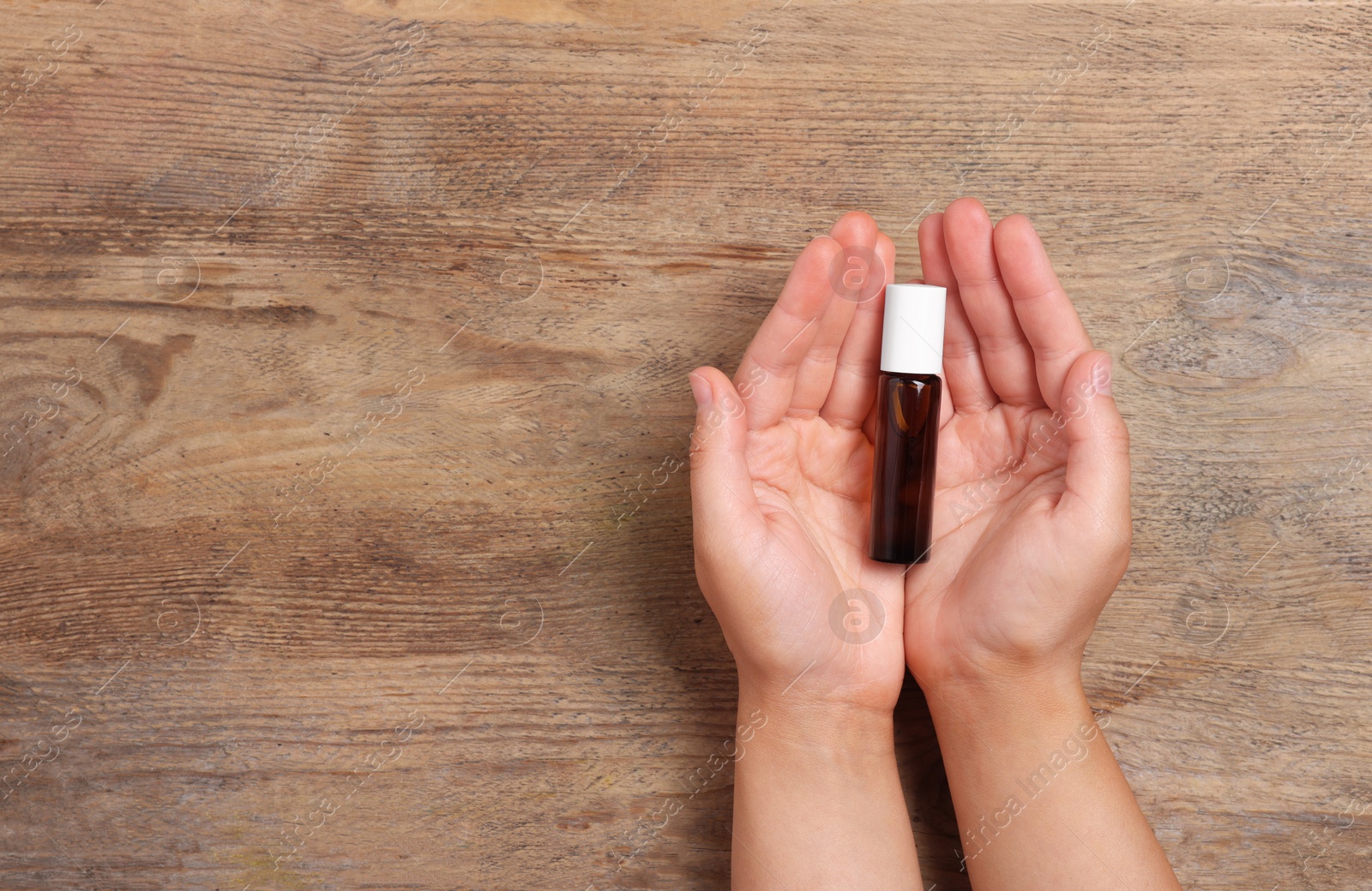 Photo of Woman with bottle of essential oil on wooden background, top view and space for text