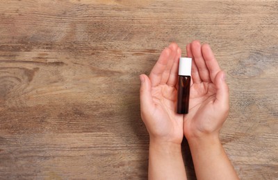 Photo of Woman with bottle of essential oil on wooden background, top view and space for text