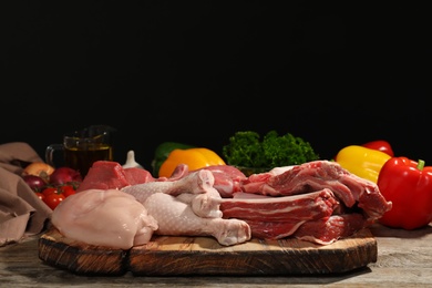 Wooden board with fresh raw meat on table against dark background