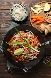 Shrimp stir fry with noodles and vegetables in wok on wooden table, flat lay