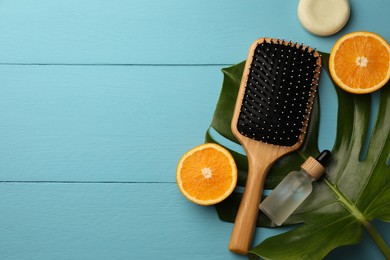Photo of Hair brush, bottle of essential oil, dry shampoo and orange slices on light blue wooden table, flat lay