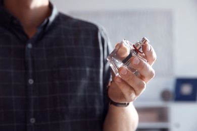 Young man with bottle of perfume indoors, closeup