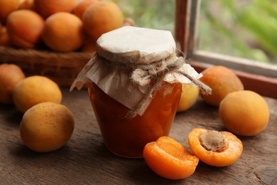 Photo of Jar of delicious jam and fresh ripe apricots on wooden table indoors. Fruit preserve