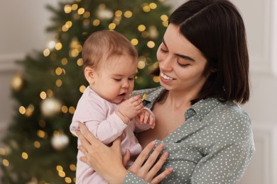 Happy young mother with her cute baby against blurred festive lights. Winter holiday