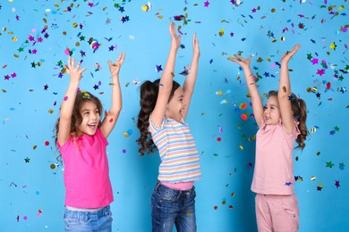 Photo of Adorable little children and falling confetti on light blue background