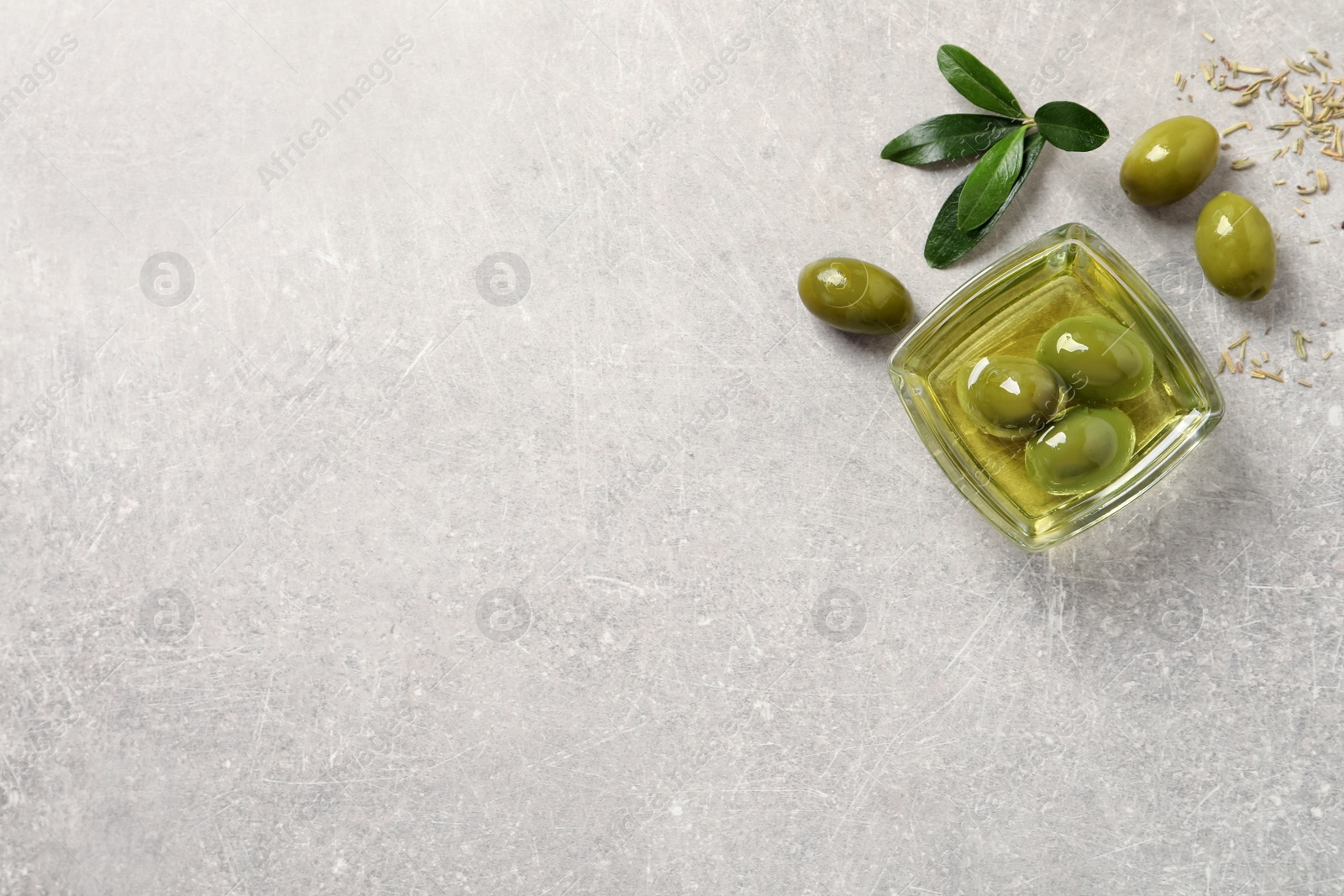 Photo of Glass bowl with fresh olive oil on light grey table, flat lay. Space for text