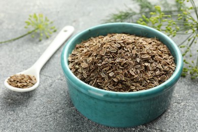 Photo of Bowl of dry seeds, spoon and fresh dill on grey table, closeup