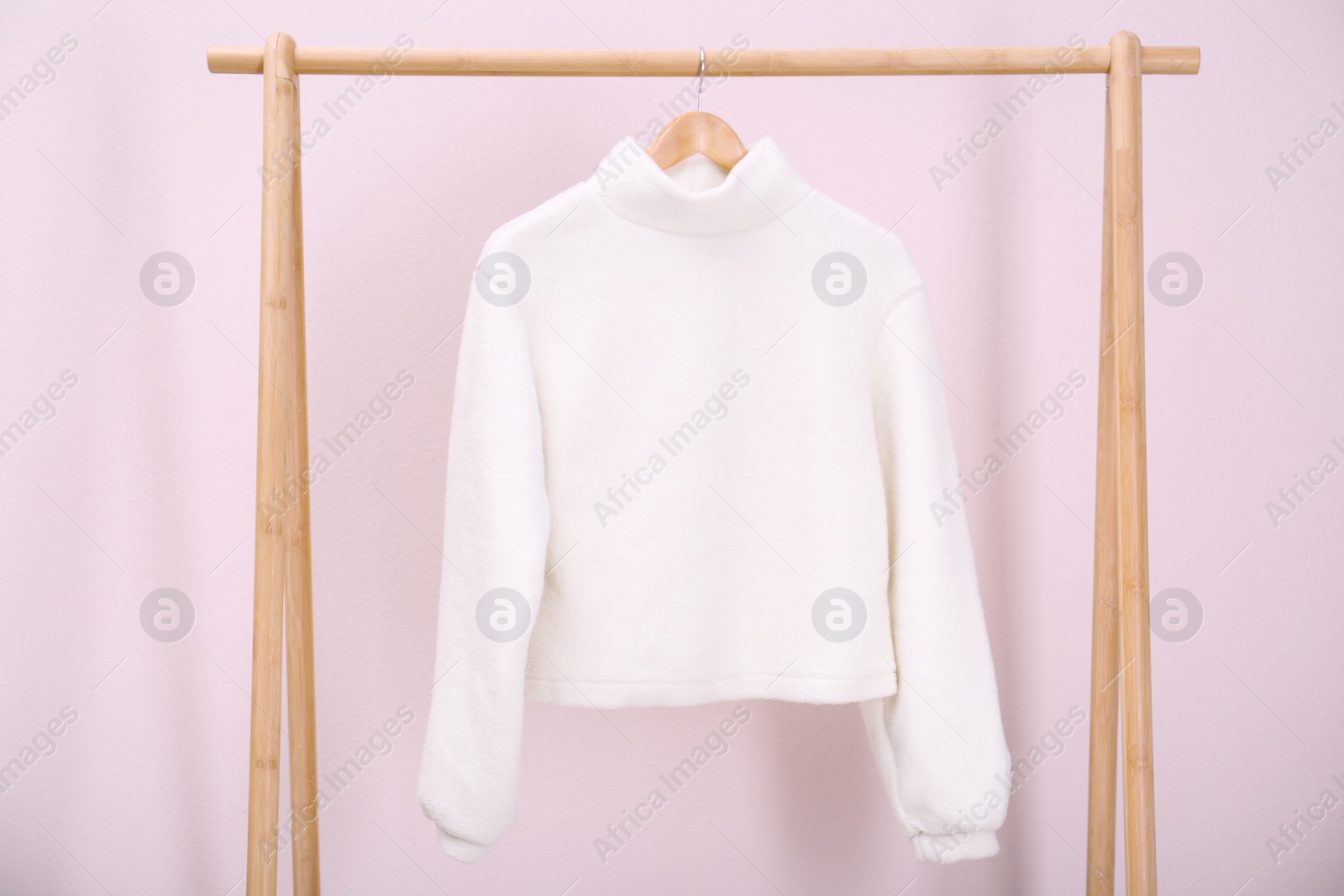 Photo of Stylish knitted sweater hanging on clothing rack near pink wall