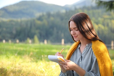 Beautiful young woman drawing with pencil in notepad outdoors on sunny day