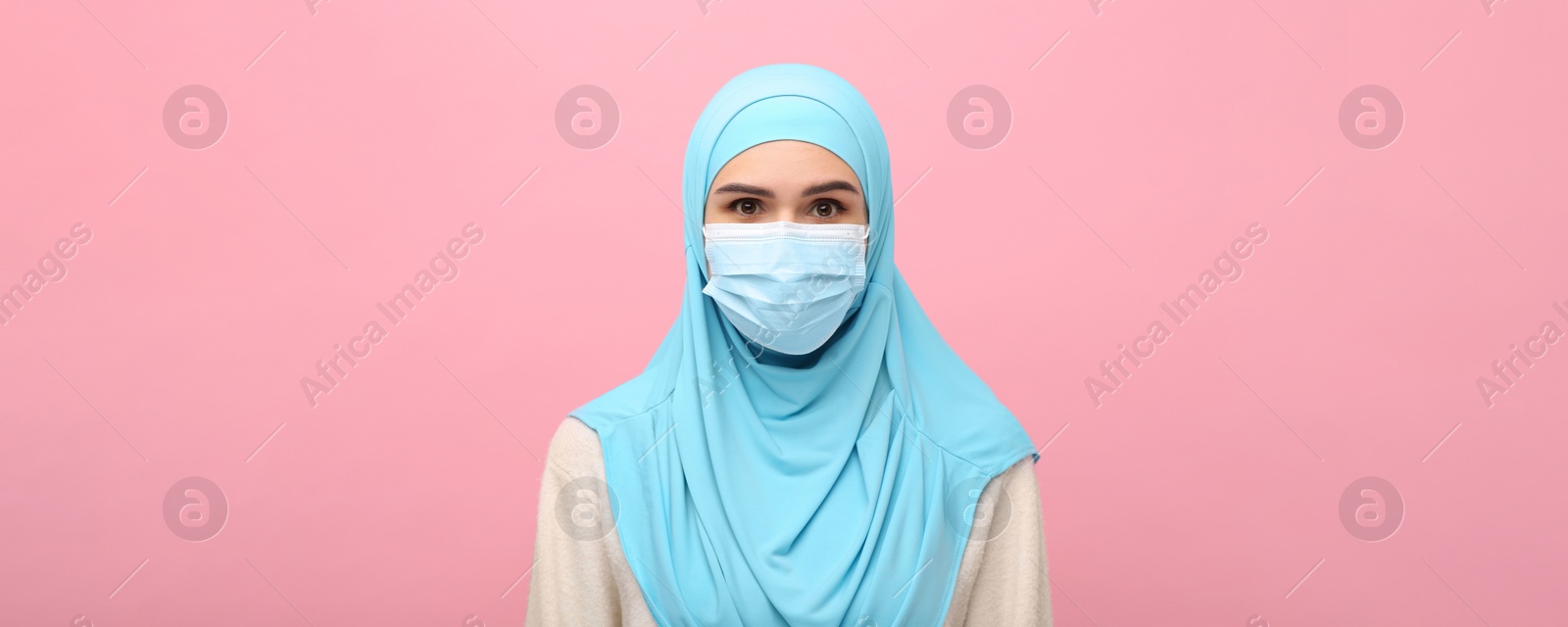 Image of Portrait of Muslim woman in hijab and medical mask on pink background. Banner design