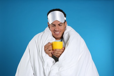 Man wrapped in blanket holding cup on blue background