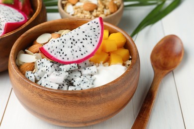 Photo of Bowl of granola with pitahaya, mango, almonds and yogurt on white wooden table