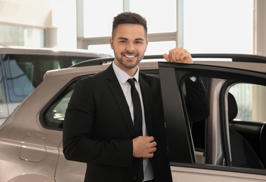 Young salesman near new car in dealership