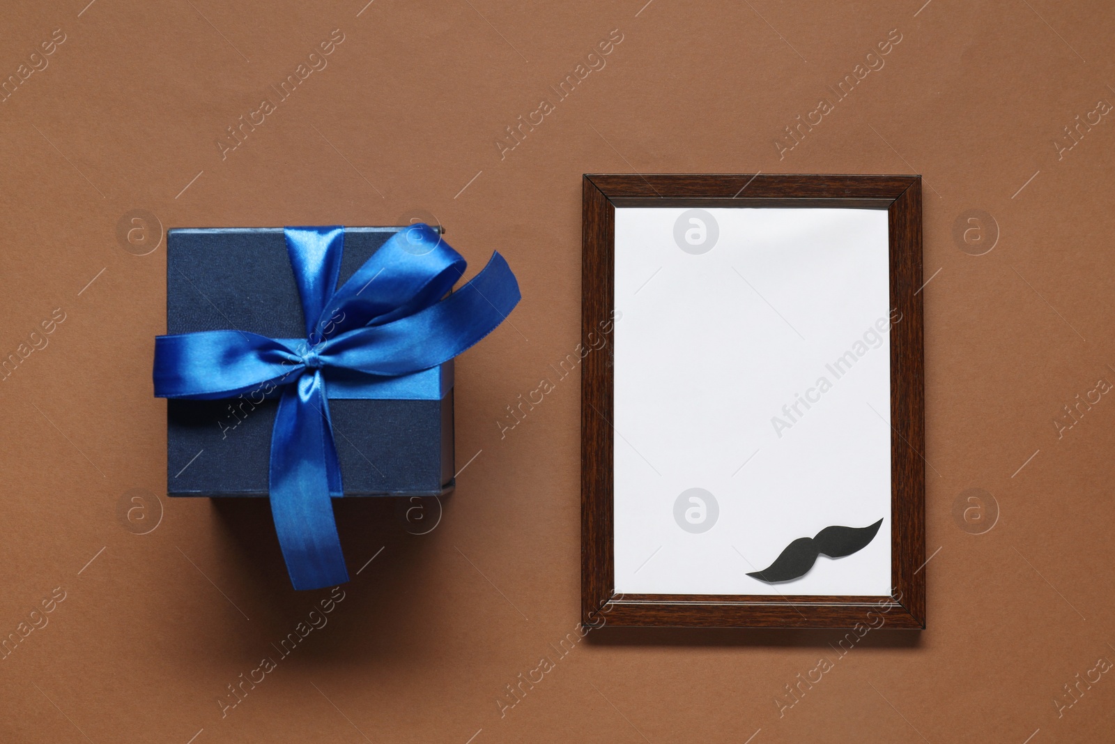 Photo of Empty photo frame and gift box on brown background, flat lay with space for text. Father's day celebration