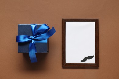 Photo of Empty photo frame and gift box on brown background, flat lay with space for text. Father's day celebration