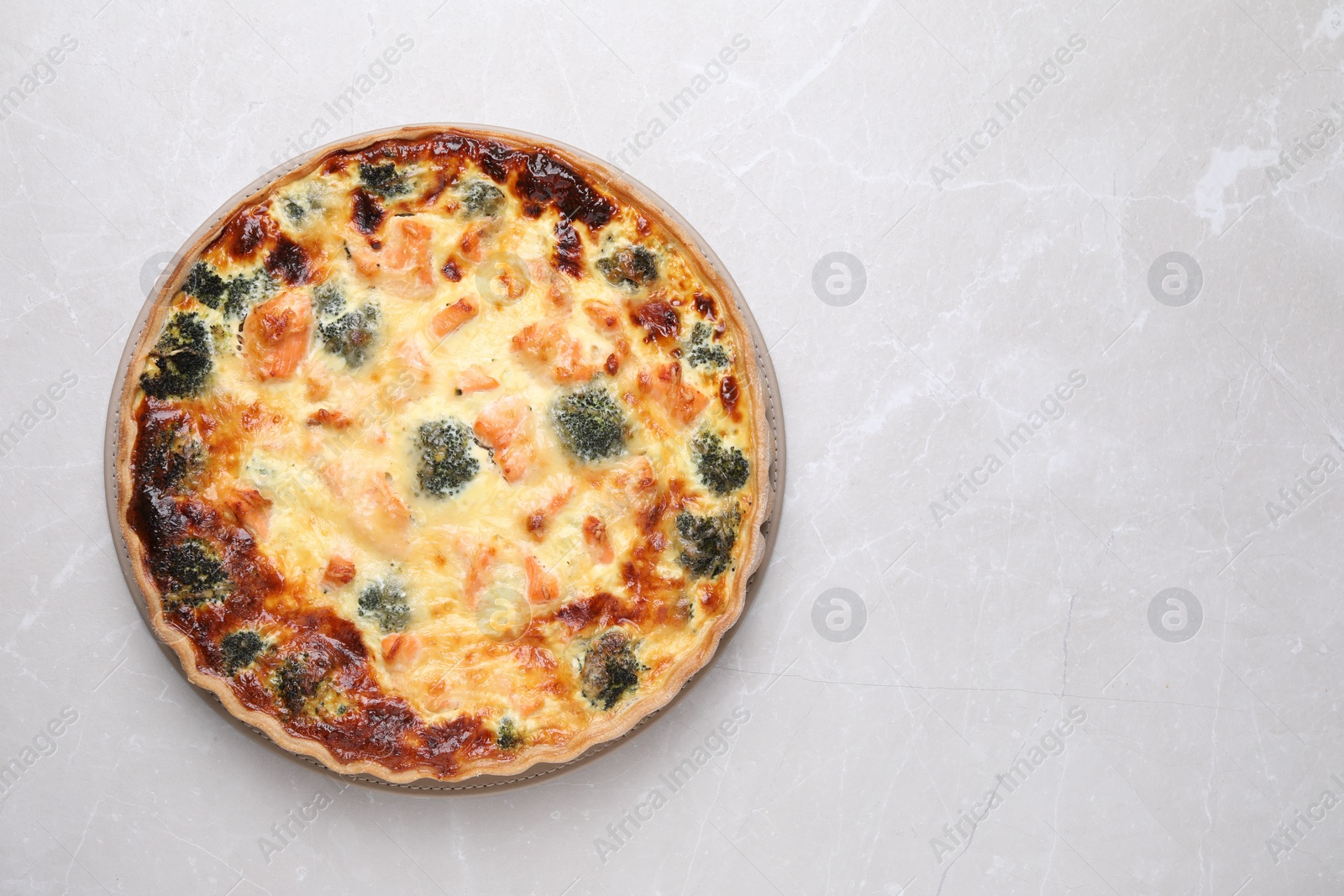 Photo of Delicious homemade quiche with salmon and broccoli on light gray marble table, top view. Space for text