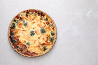 Photo of Delicious homemade quiche with salmon and broccoli on light gray marble table, top view. Space for text