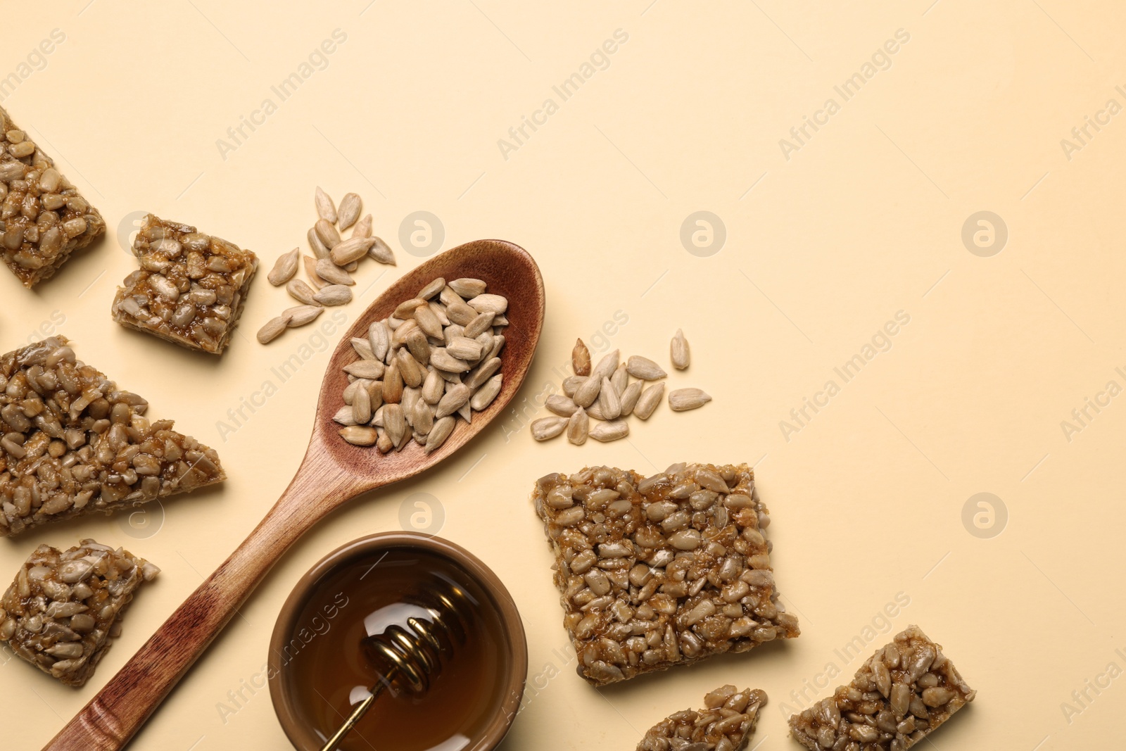 Photo of Pieces of delicious kozinaki bars, honey and sunflower seeds on beige background, flat lay. Space for text