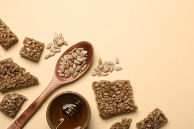 Photo of Pieces of delicious kozinaki bars, honey and sunflower seeds on beige background, flat lay. Space for text