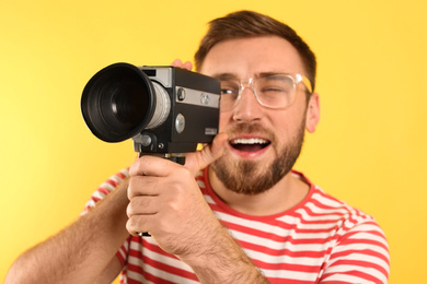 Photo of Young man with vintage video camera on yellow background, focus on lens