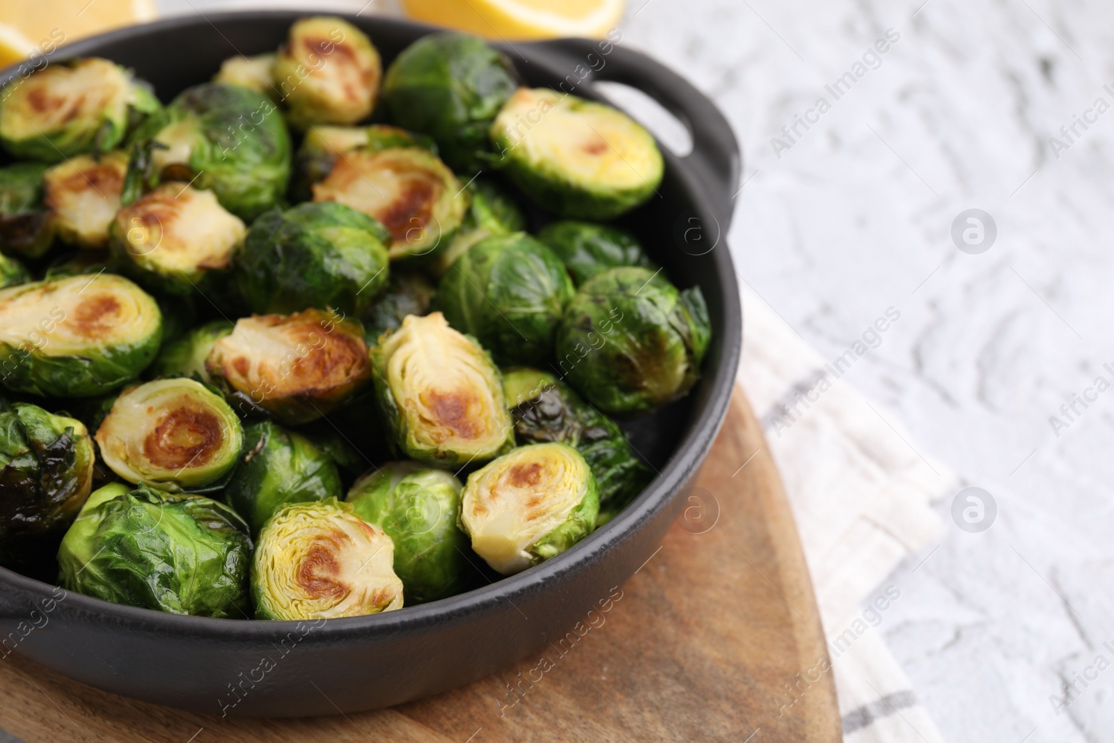 Photo of Delicious roasted Brussels sprouts in baking dish on white textured table, closeup. Space for text