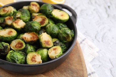 Delicious roasted Brussels sprouts in baking dish on white textured table, closeup. Space for text