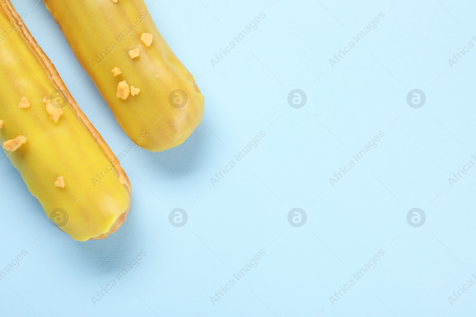 Photo of Delicious eclairs covered with glaze on light blue background, top view. Space for text