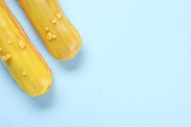 Photo of Delicious eclairs covered with glaze on light blue background, top view. Space for text