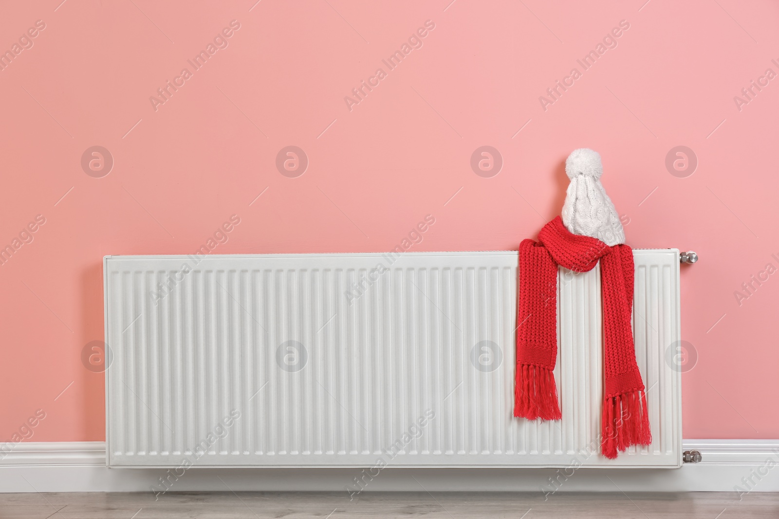 Photo of Heating radiator with knitted cap and scarf near color wall. Space for text