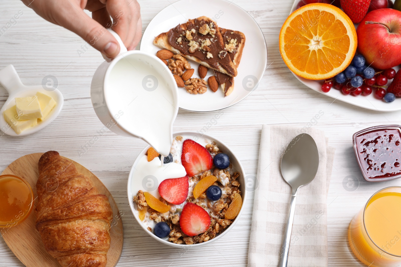 Photo of Man pouring greek yoghurt into granola at white wooden table, top view