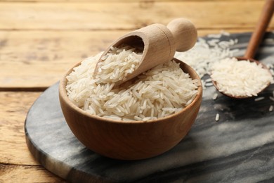 Photo of Raw basmati rice in bowl, scoop and spoon on wooden table, closeup