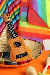 Mexican sombrero hat, ukulele and maracas on orange table, closeup