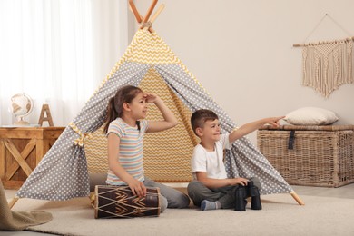 Photo of Cute little children playing in toy wigwam at home