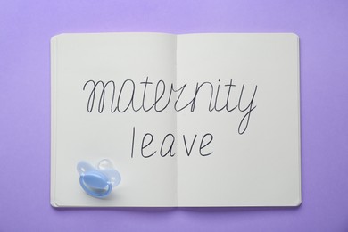 Photo of Notebook with phrase Maternity Leave and pacifier on violet background, top view