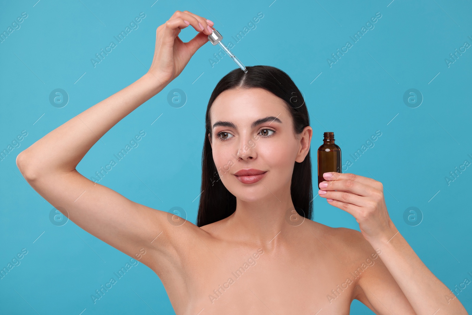 Photo of Beautiful woman applying hair serum on light blue background. Cosmetic product